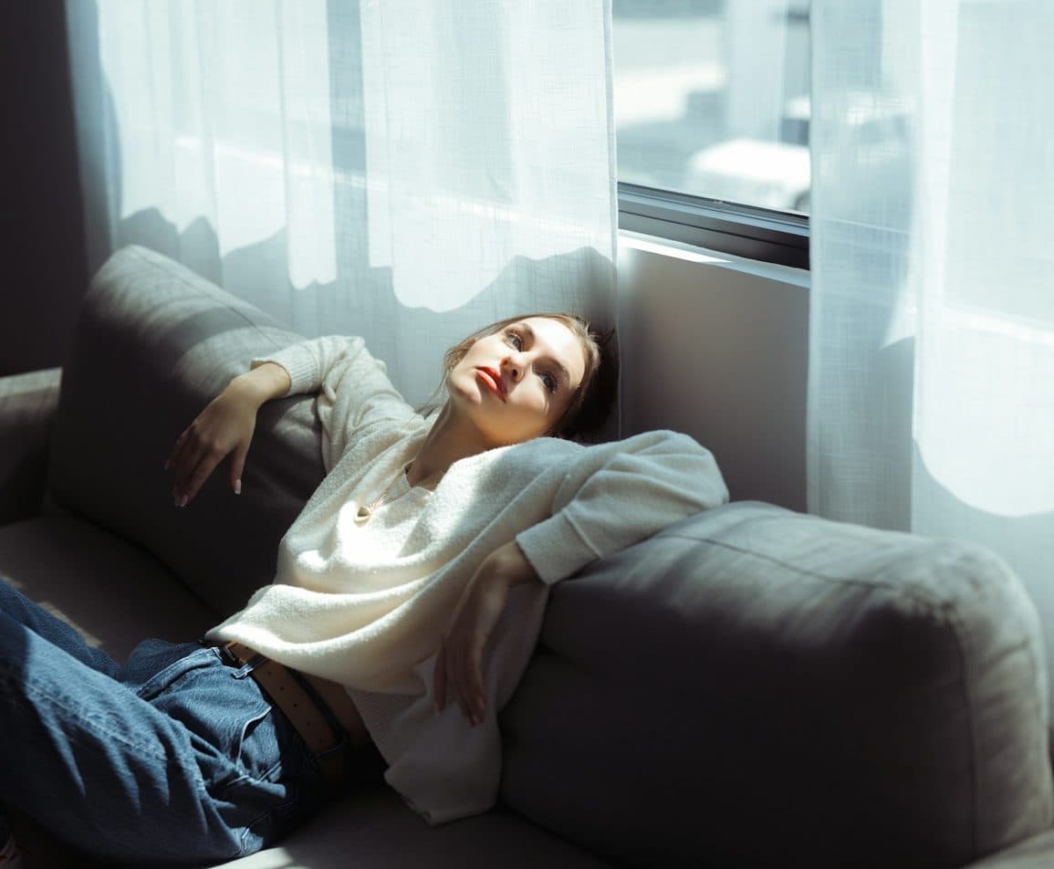 Woman relaxing on a grey sofa by a bright window